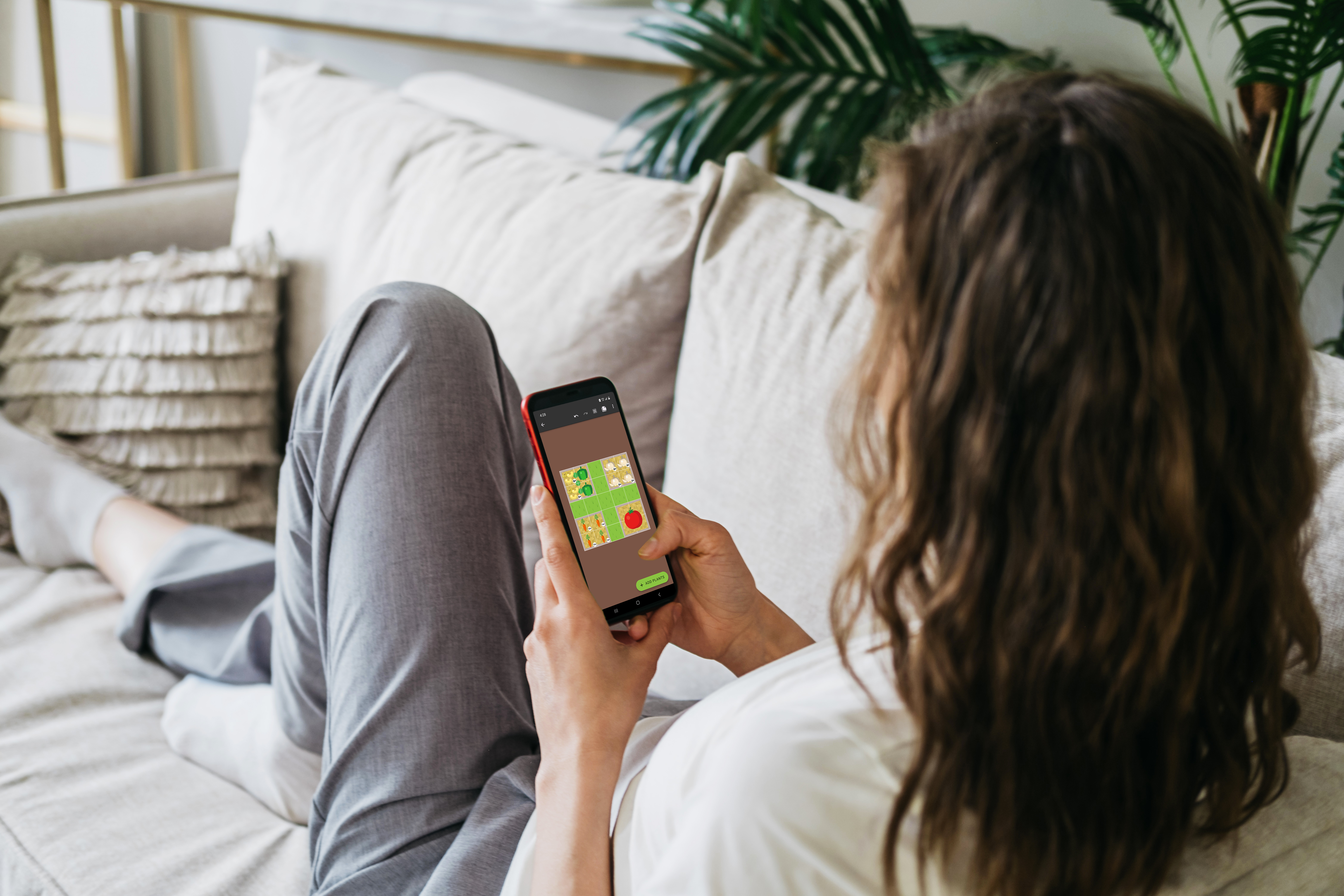 A girl sitting on a couch facing sideways holding a phone with the Planter app on it