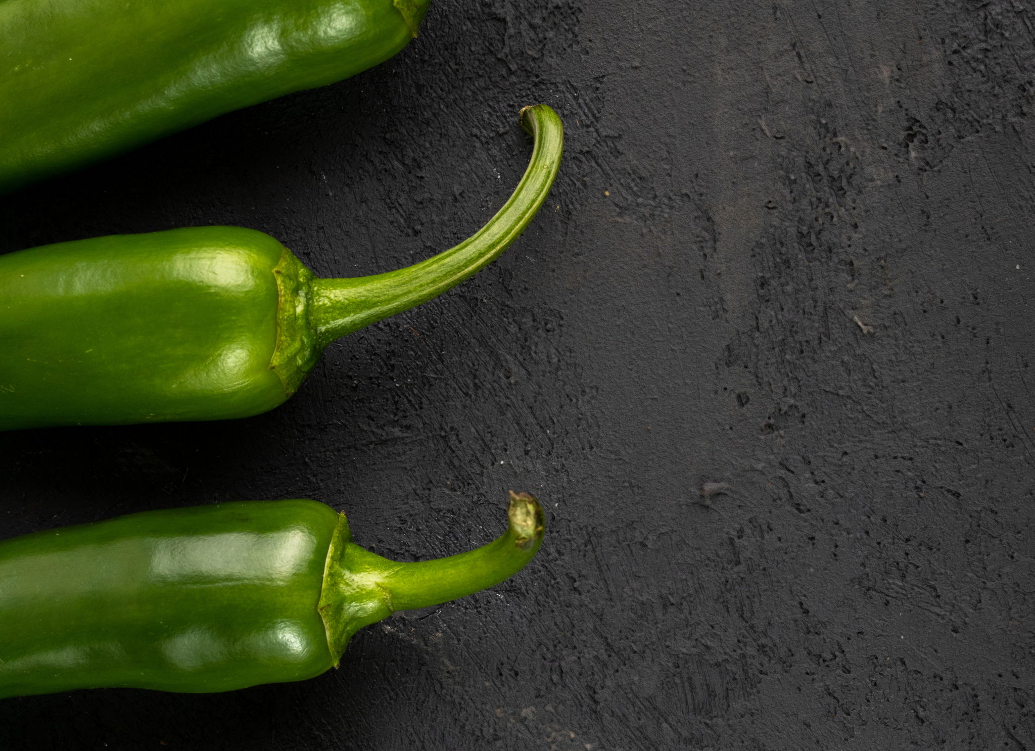 Three jalapeño peppers on the left-hand side with a black background.