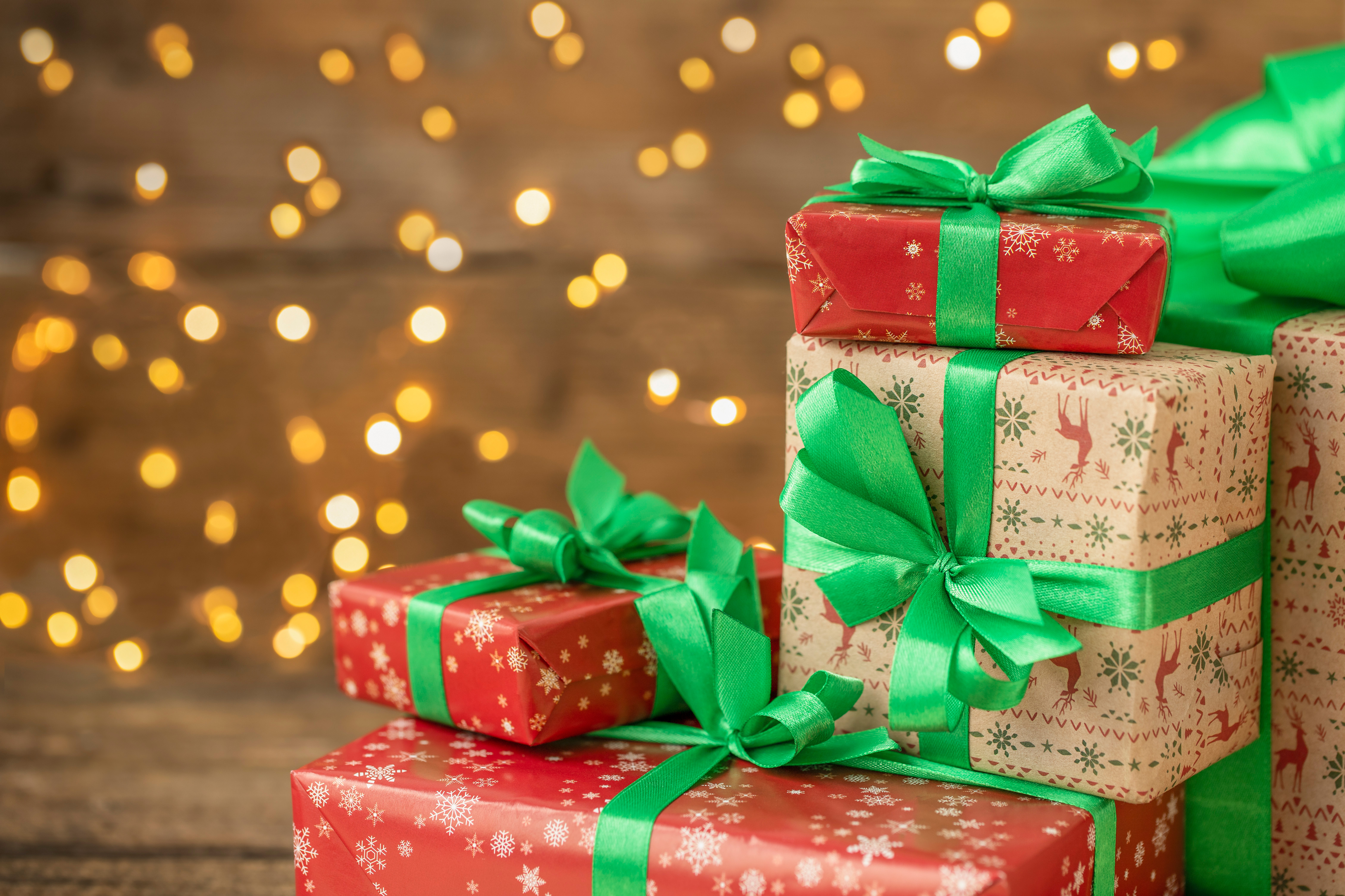 Christmas gifts with red and brown wrapping paper and green bows with faded twinkle lights in the background