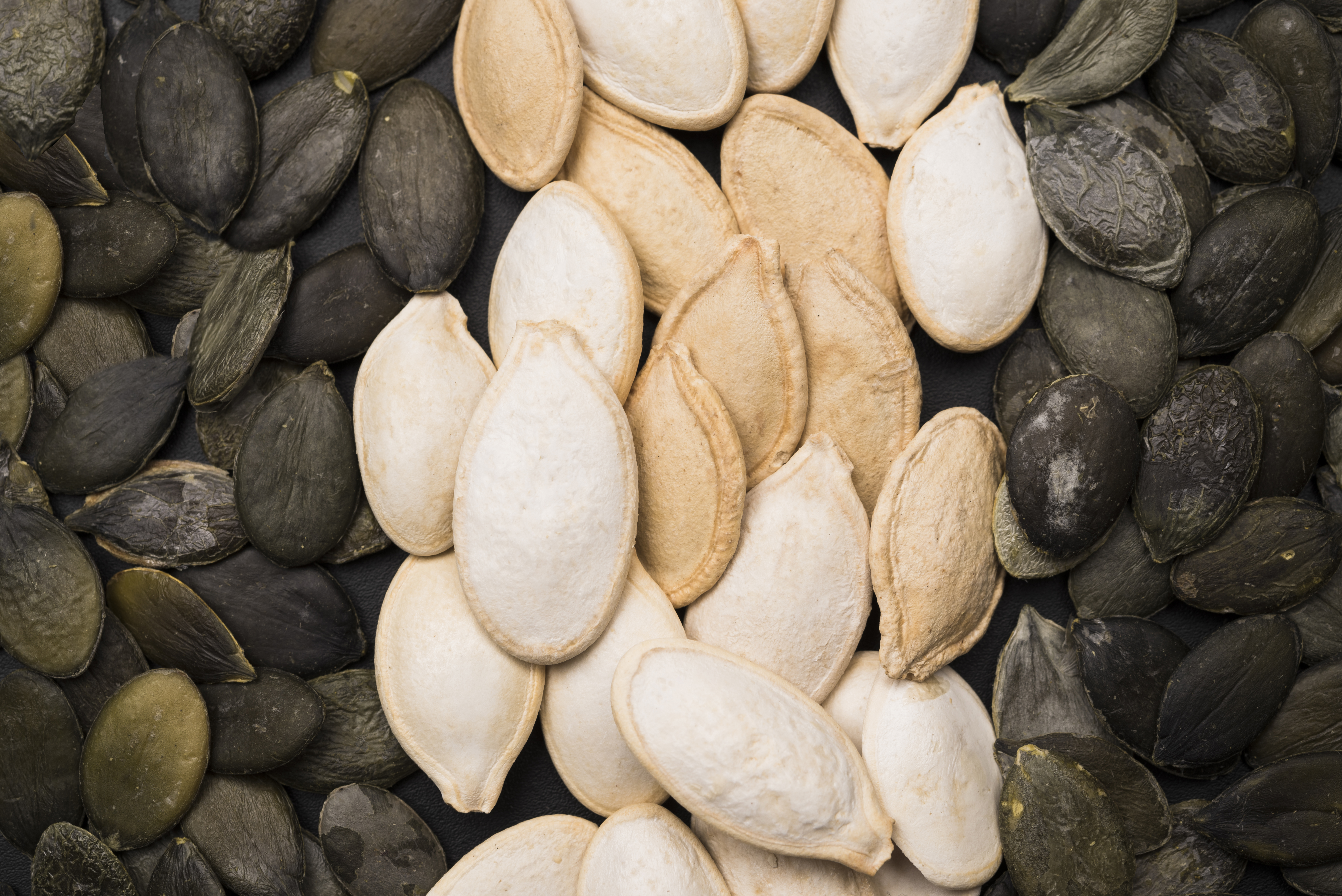 Close up photo of seeds from the squash family. There is a column of overlapping white seeds in the middle, and a column of overlapping black seeds on either side.